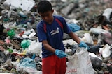 A boy, surrounded by a pile of trash, scavenges for plastic for recycling at a garbage dump site.