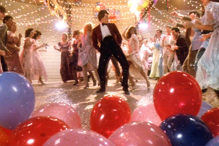 Kevin Bacon in a red suit dancing in a prom scene of the movie