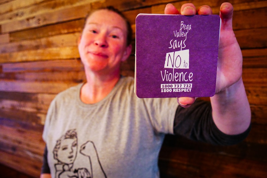 Woman holding a purple coaster up to the camera with message 'Bega Valley says no to violence'