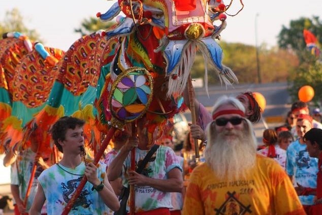 A manin a beard with a brightly coloured Chinese dragon behind