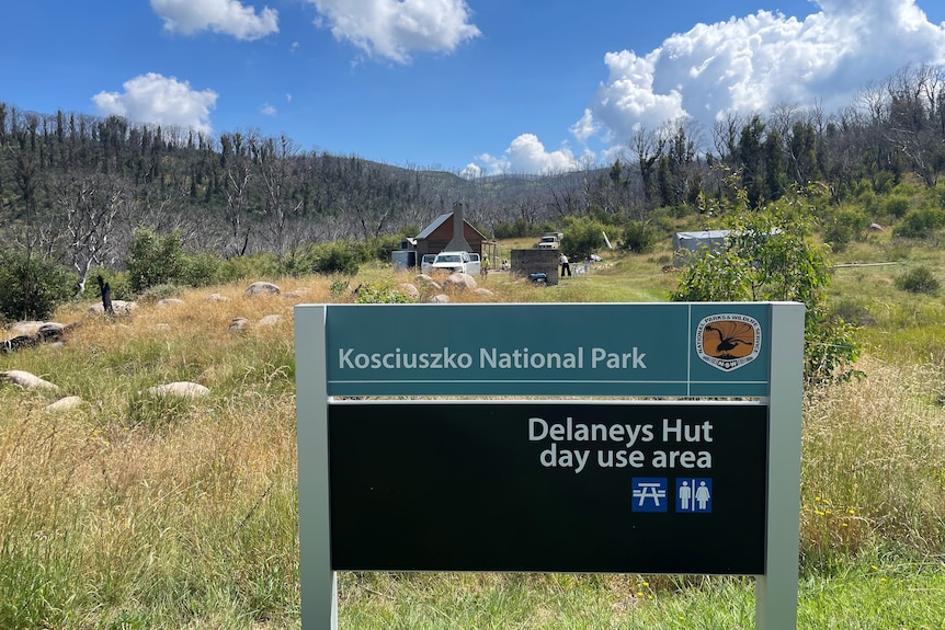 A national park sign with a hut in the background surrounded by hills