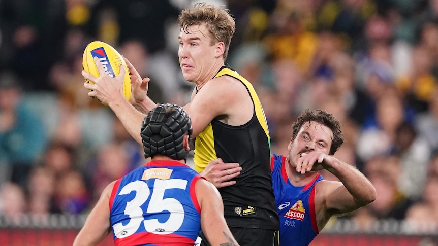 A Richmond AFL player marks the ball with two Western Bulldogs opponents near him.