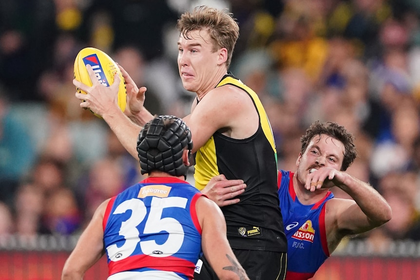 A Richmond AFL player marks the ball with two Western Bulldogs opponents near him.