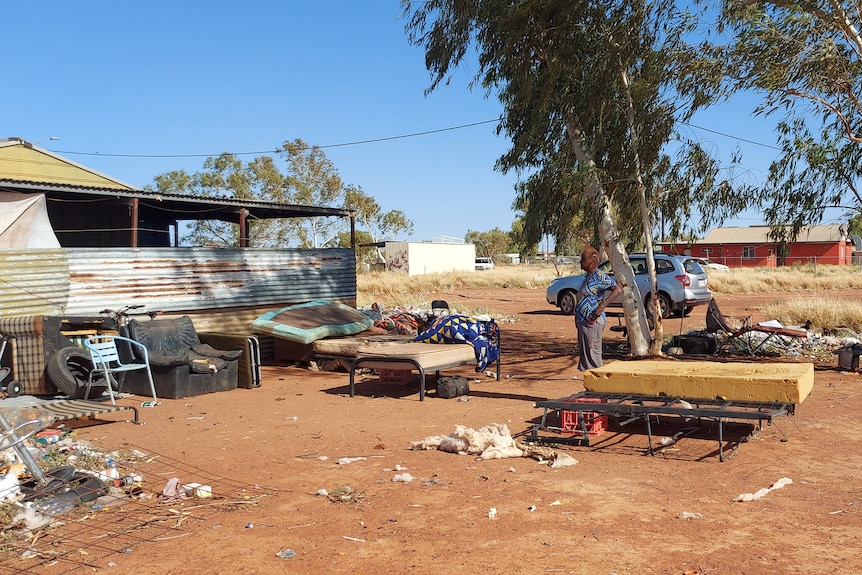 A woman looking at a ramshackle house made of corrugated iron, in a remote community.