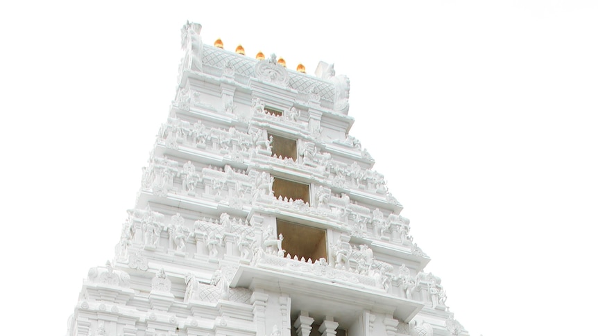 White Hindu temple towers into the sky with 5 golden pots sitting on the roof