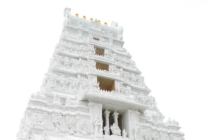 White Hindu temple towers into the sky with 5 golden pots sitting on the roof