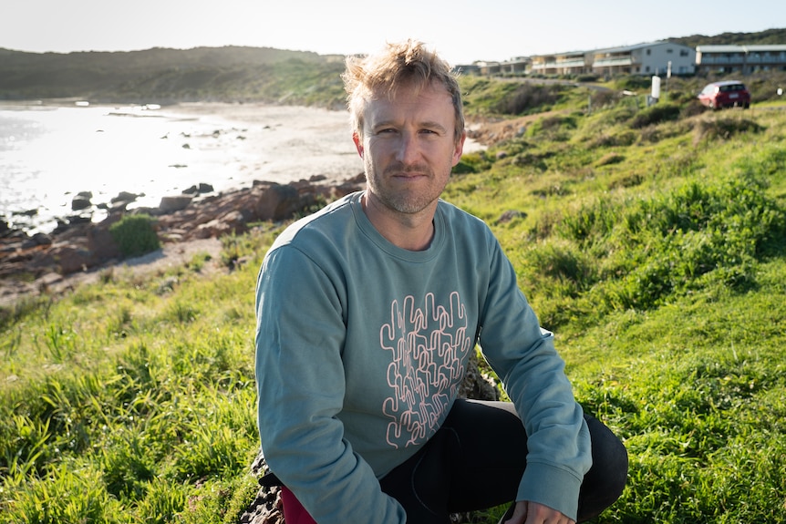 A man sits on grass near a beach.