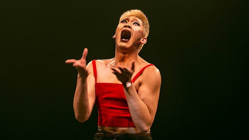 Close-up of a vogue dancer in dramatic makeup and red shirt with open mouth and wide eyes on stage at Sissy Ball 2019.