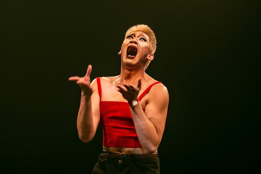 Close-up of a vogue dancer in dramatic makeup and red shirt with open mouth and wide eyes on stage at Sissy Ball 2019.