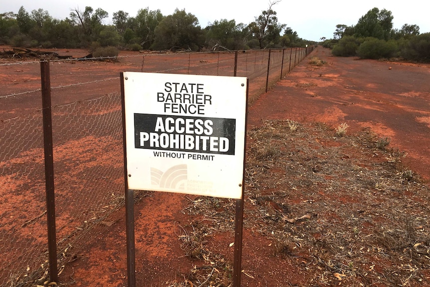 A sign prohibiting access on a fence surrounded by red dirt.