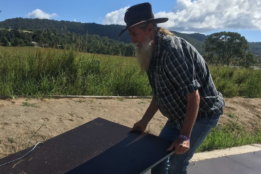 David Bauer with long beard and wizard hat lifts a large piece of steel sheet.