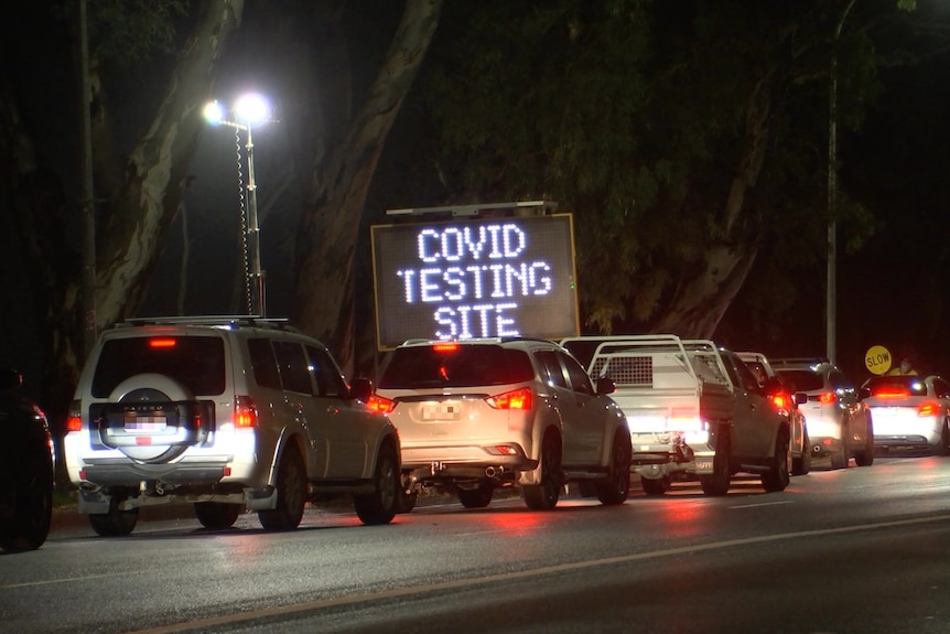 Cars lining up at night with an electronic sign saying COVID TESTING SITE