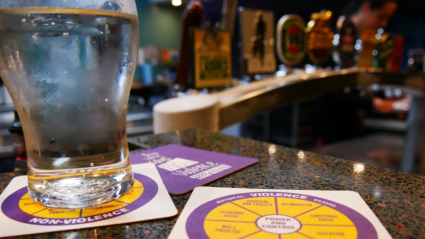 Close up shot of drink coasters on a pub bar with a diagram of the signs of violent and non-violent relationships