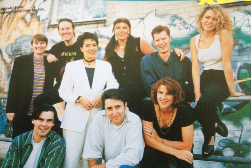 Group of young men and women standing in front of a wall with graffiti painted on it.