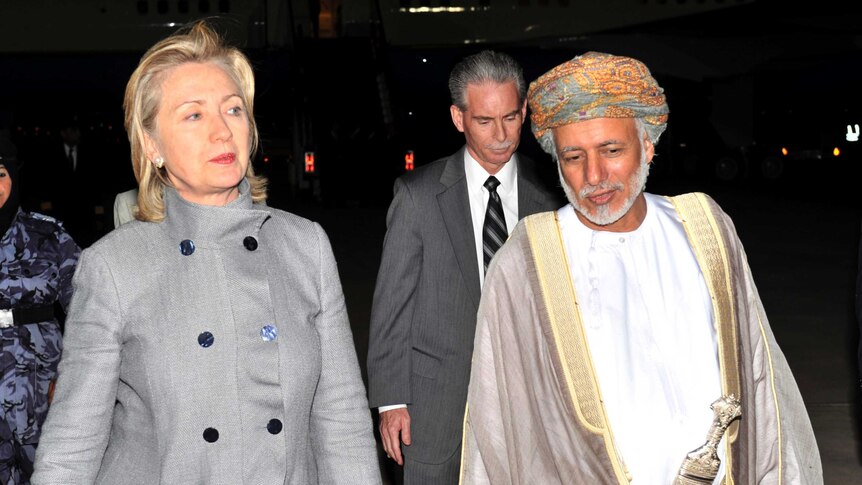 Hilary Clinton walks beside Sultan Qaboos bin Said, who wears a multi-coloured turban and carries an ornate dagger.