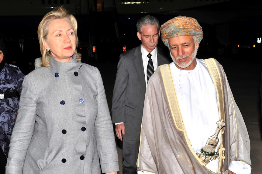 Hilary Clinton walks beside Sultan Qaboos bin Said, who wears a multi-coloured turban and carries an ornate dagger.