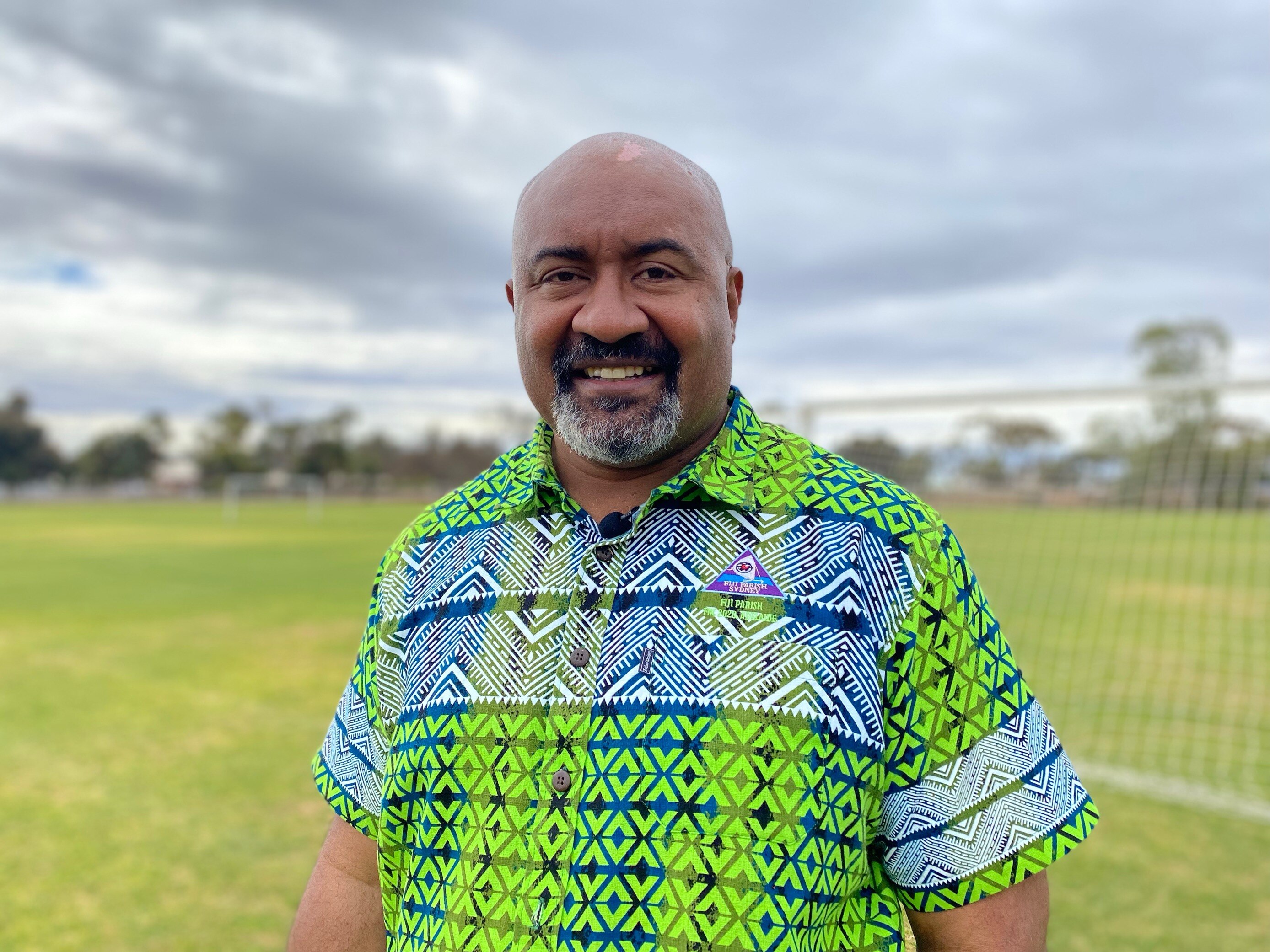 A bald man with a green and blue shirt standing in a field