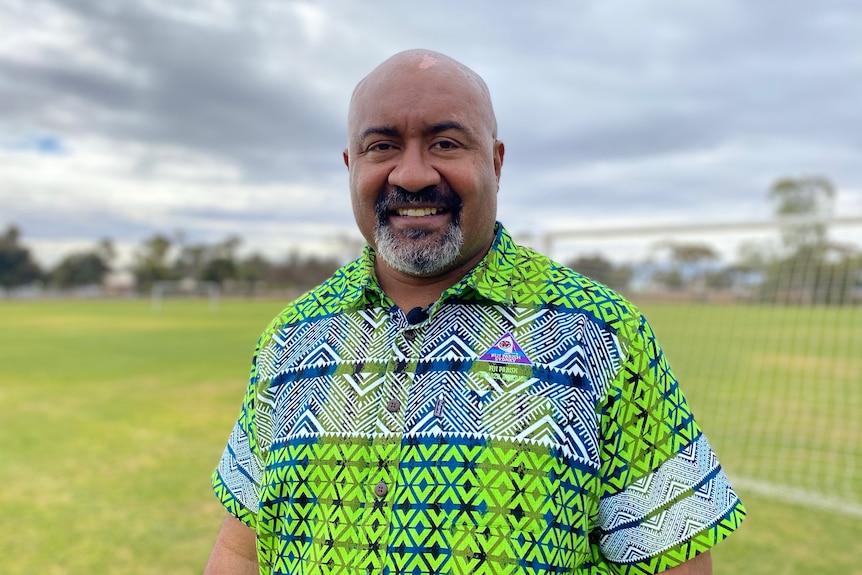 A bald man with a green and blue shirt standing in a field