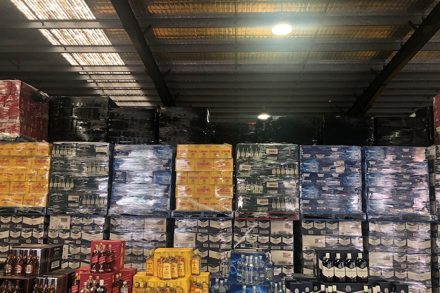 Large plastic-wrapped boxes of alcohol are stacked and assembled in a warehouse.