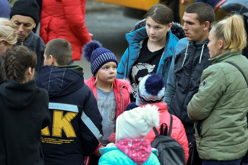 Two adults talk to four children as other people move about nearby,