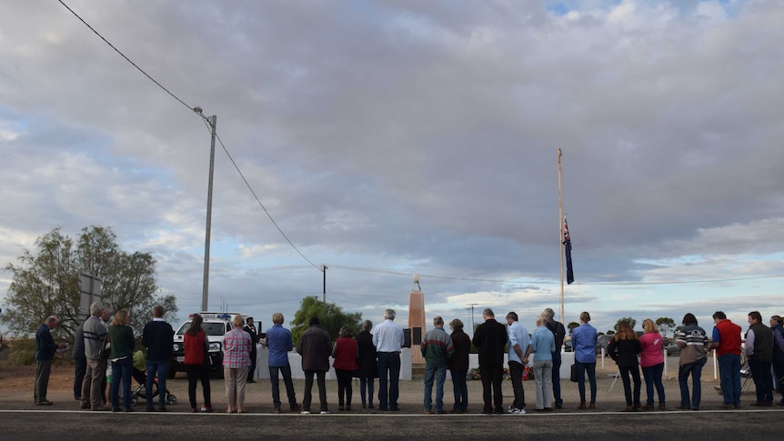 A line of people stands in front of a war memorial.