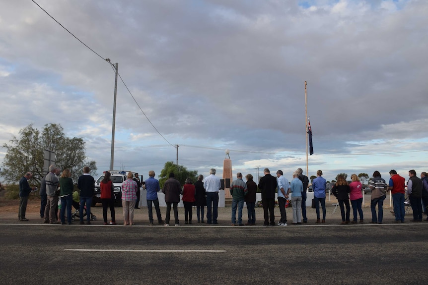 A line of people stands in front of a war memorial.