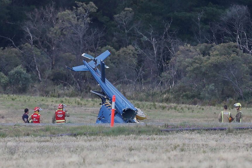 Wreckage of a blue helicopter on a tarmac.