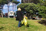 A woman carries yellow ribbons in a park.
