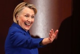 Hillary Clinton wearing a blue coat and smiling and waving.