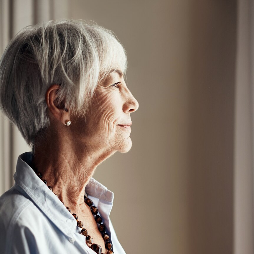 side view of an older woman looking thoughtfully out of a window