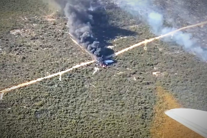 A plane on fire in low green scrub lane