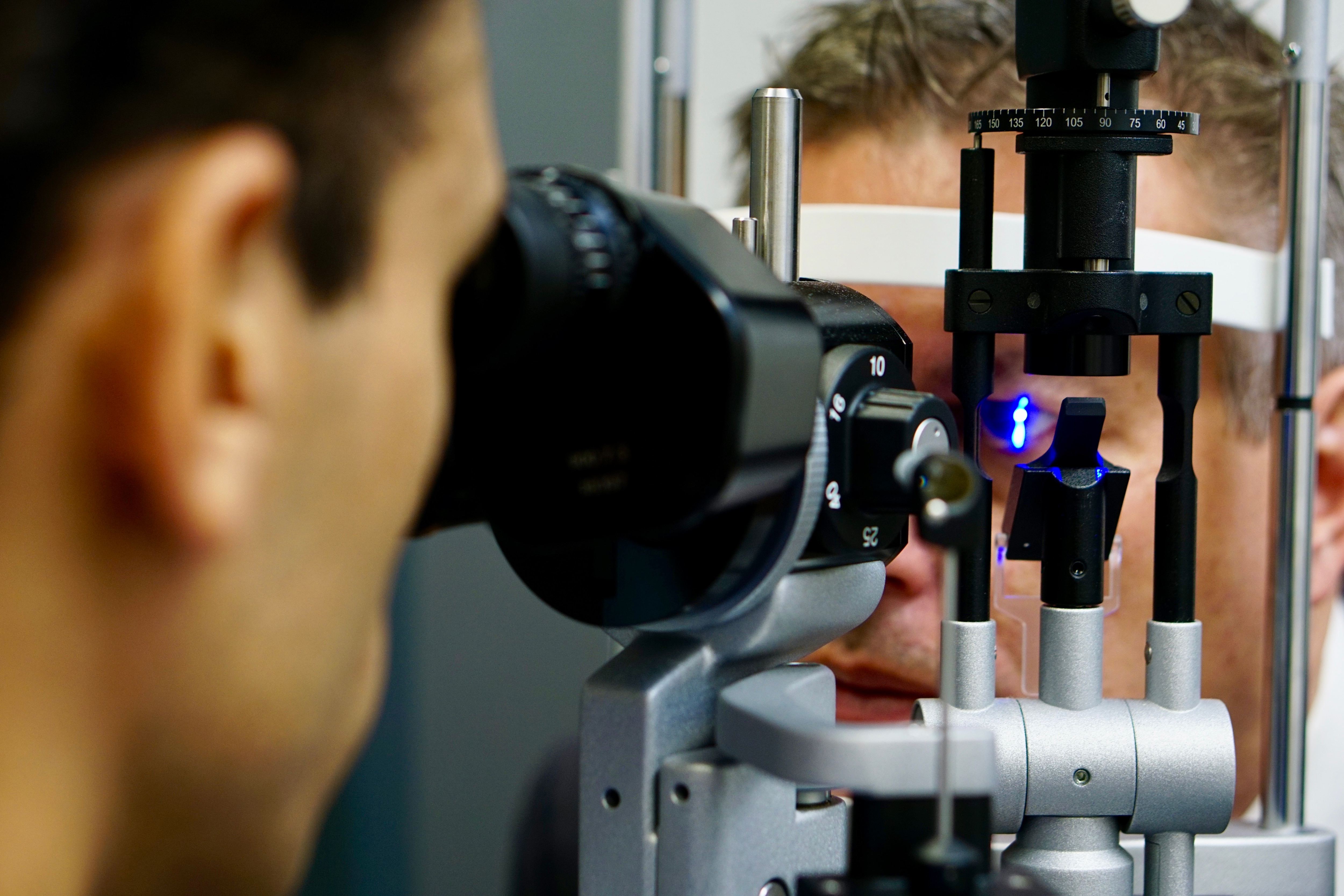 एक आदमी नीली रोशनी से किसी की आंखों का विश्लेषण करने के लिए उपकरण का उपयोग करता है।