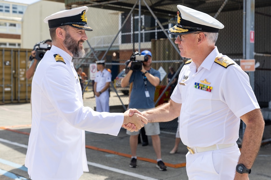 Two men in navy uniform shake hands