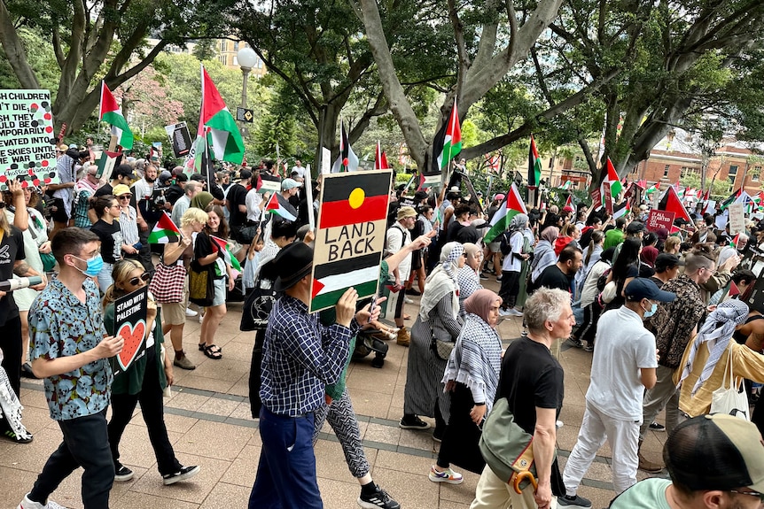Protesters march at a pro-Palestinian rally, a placard in the centre has the Palestinan and Aboriginal flag with text land back