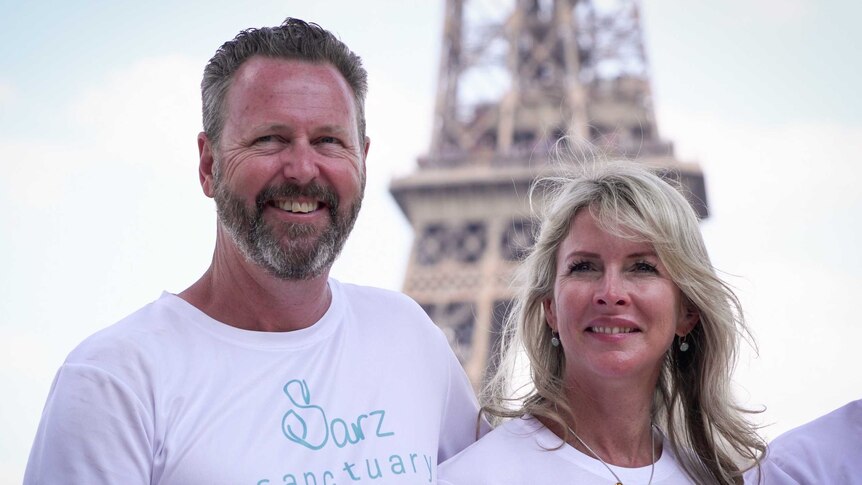 Parents hold up Australian flag in front of Eiffel Tower.