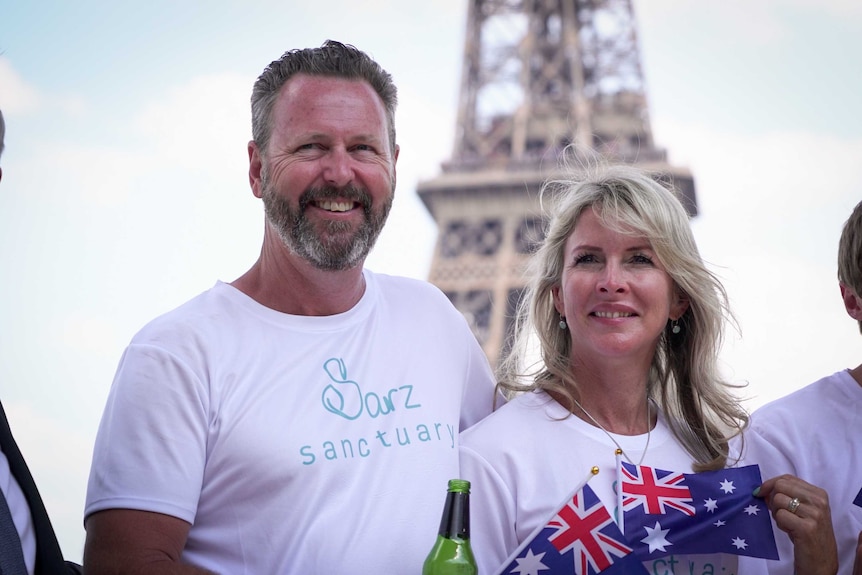 Parents hold up Australian flag in front of Eiffel Tower.