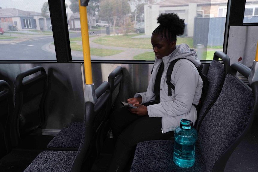 Teenage girl in a puffer jacket sits on a bus looking at her phone