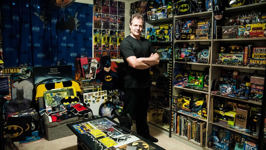 A man standing with arms crossed in a room full of products and toys all relating to Batman