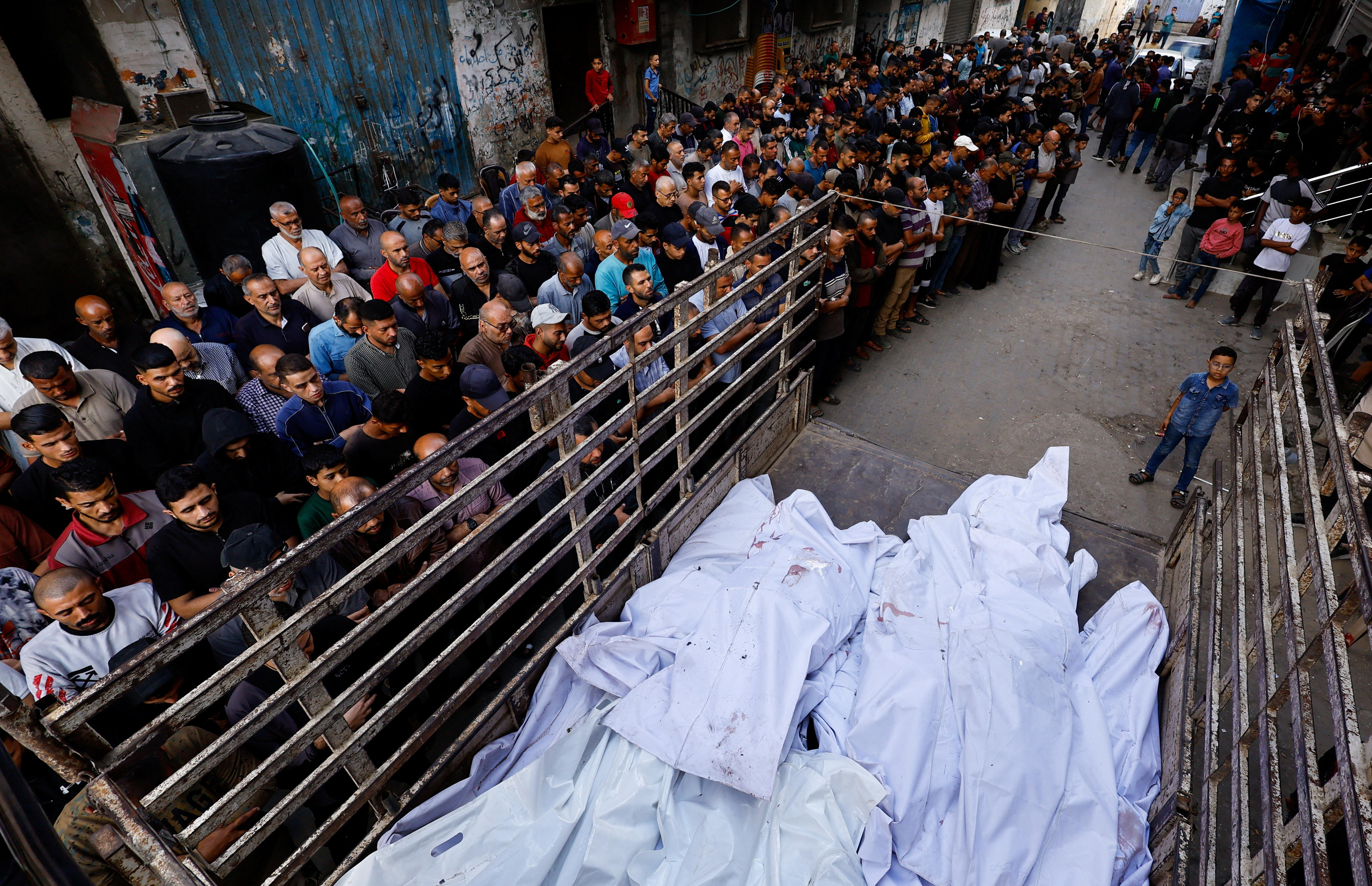 Rows of people line a truck filled with white shrouds