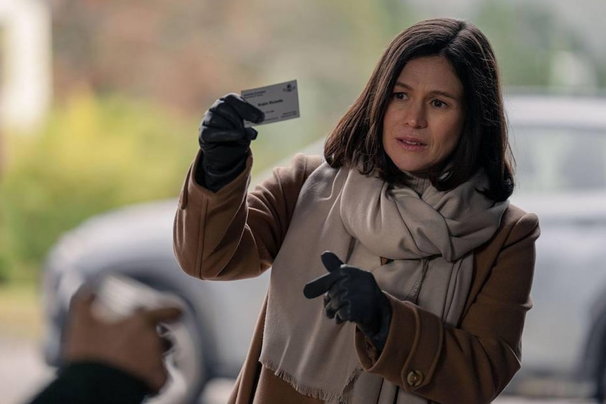 A woman wearing a coat, scarf and gloves holds up a business card.