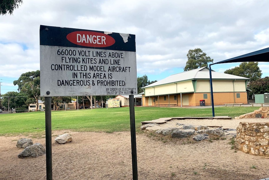 A sign warns against the usage of kites and model aircraft at a school oval due to 66,000 volt cables.