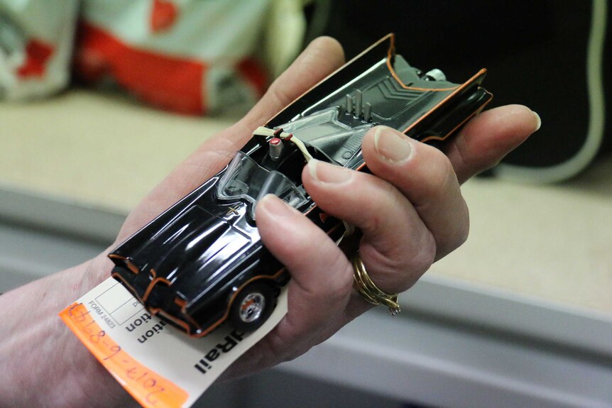 Hand holds up a small 1960s Batmobile toy