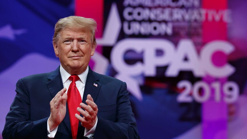 Trump stand clapping in front of CPAC poster