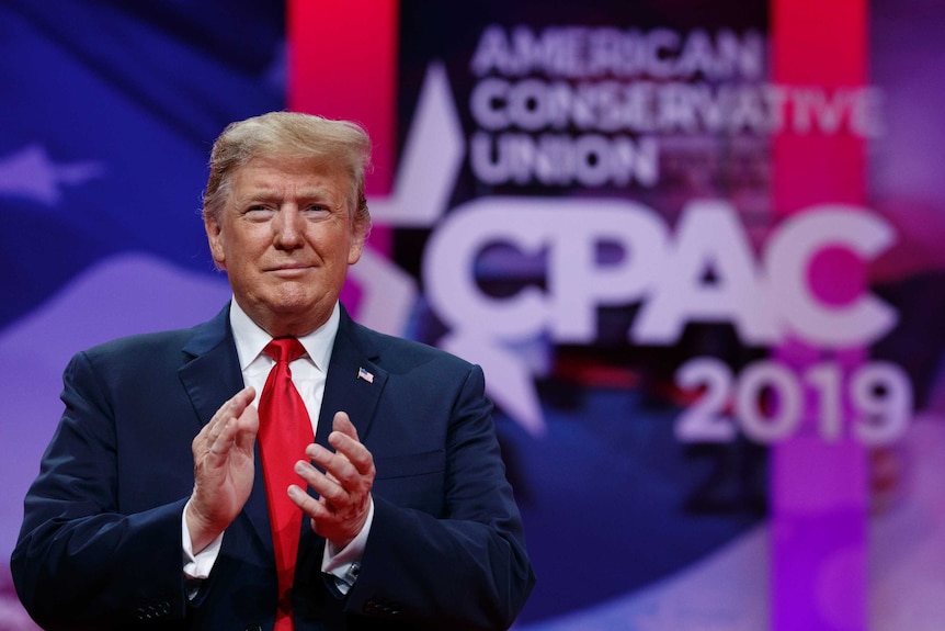 Trump stand clapping in front of CPAC poster