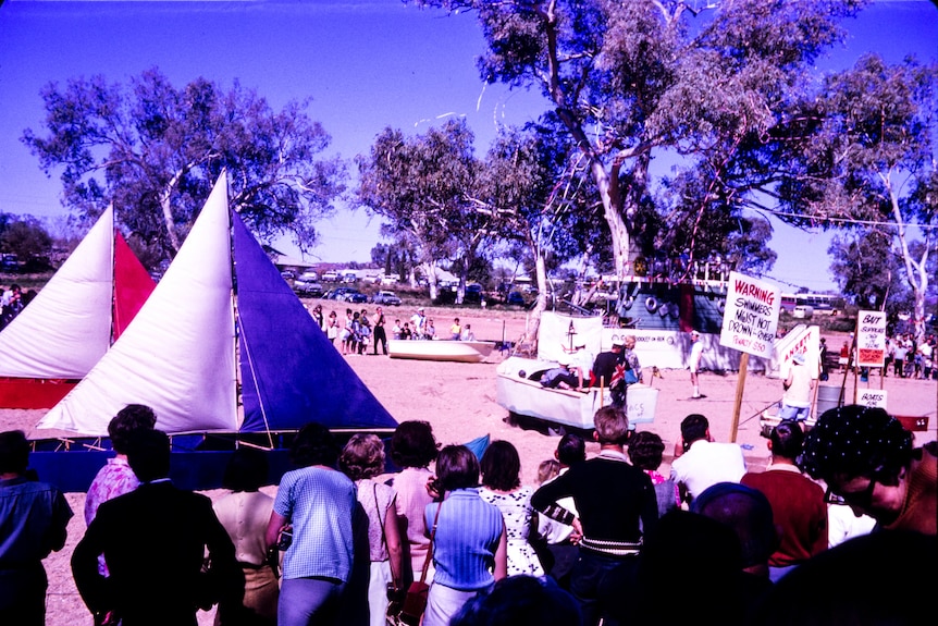 A historic photograph shows makeshift boats being carried across a sandy riverbed.