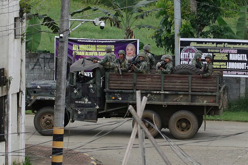 A truck-load of Philippines soldiers, guns raised, drives through a deserted Marawi street.