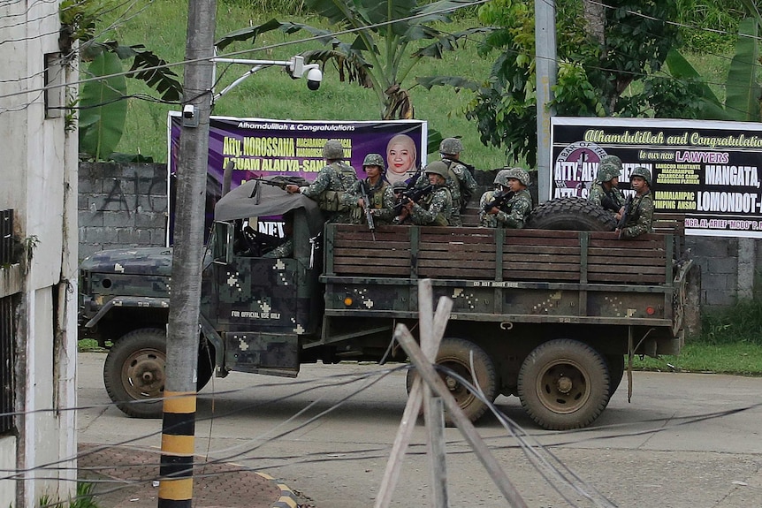 A truck-load of Philippines soldiers, guns raised, drives through a deserted Marawi street.