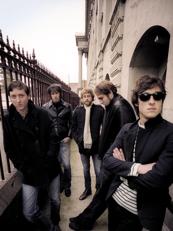 A press shot of The Panics posing in an English-style front yard with guarded rail