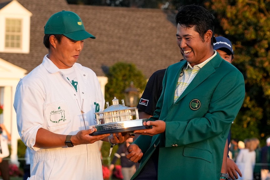 Hideki Matsuyama and caddy Shota Hayafuji looks down at the Masters trophy, which they are holding