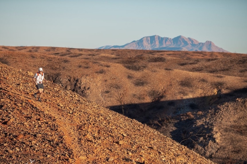 small runner in foreground on denuded red landscape with large mountain in far distance